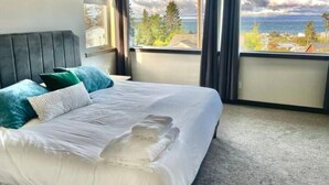 A hotel room with a large bed, a headboard, and a view of the ocean and trees through the windows.