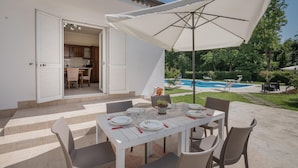 An outdoor dining area with a table set for four, a white umbrella, and a view of a swimming pool. - Awesome home in Villa S. Lucia (Villa S. Lucia)
