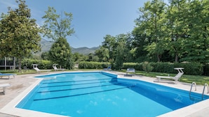 A rectangular swimming pool with clear blue water, surrounded by lounge chairs and a landscaped garden with trees and shrubs. - Awesome home in Villa S. Lucia (Villa S. Lucia)