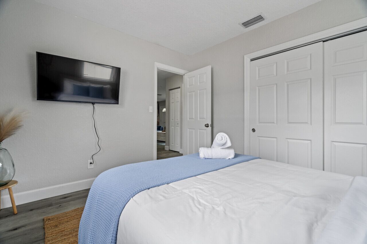 A bedroom with a bed, a TV mounted on the wall, and a door leading to another room.