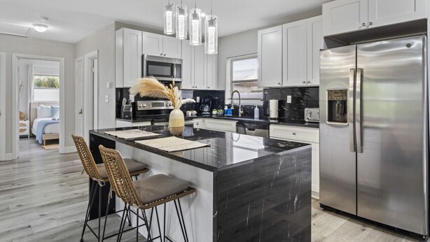 A modern kitchen with white cabinets, a stainless steel refrigerator, and a central island with bar stools.