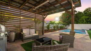 An outdoor patio with wicker furniture, a grill, and a pool.