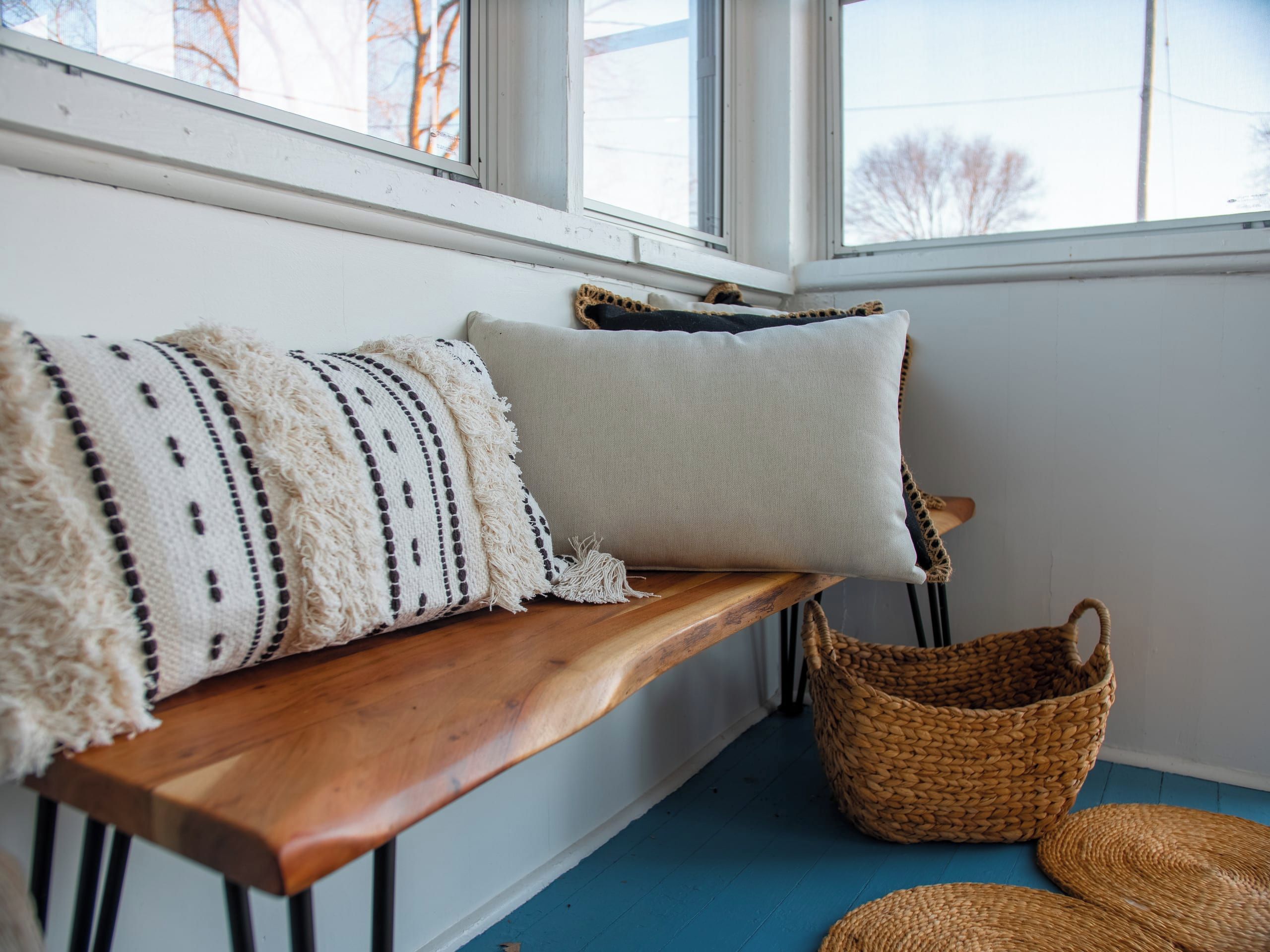 Un banc en bois avec deux coussins, un panier tressé et un tapis tressé, le tout posé sur un sol bleu.