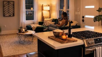 Una cocina moderna con una isla central, un comedor con sofá y una sala de estar con una persona sentada.