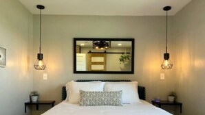 A neatly made bed with a white comforter and two pillows, flanked by two bedside tables with lamps, in a room with a large mirror above the bed. - [C] Private Country Retreat 10 Acres + 4 Min to Lawrence (Lawrence)