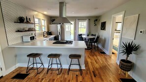 A modern kitchen with a central island, bar stools, a dining area with a table and chairs, and a large window providing natural light. - [C] Private Country Retreat 10 Acres + 4 Min to Lawrence (Lawrence)