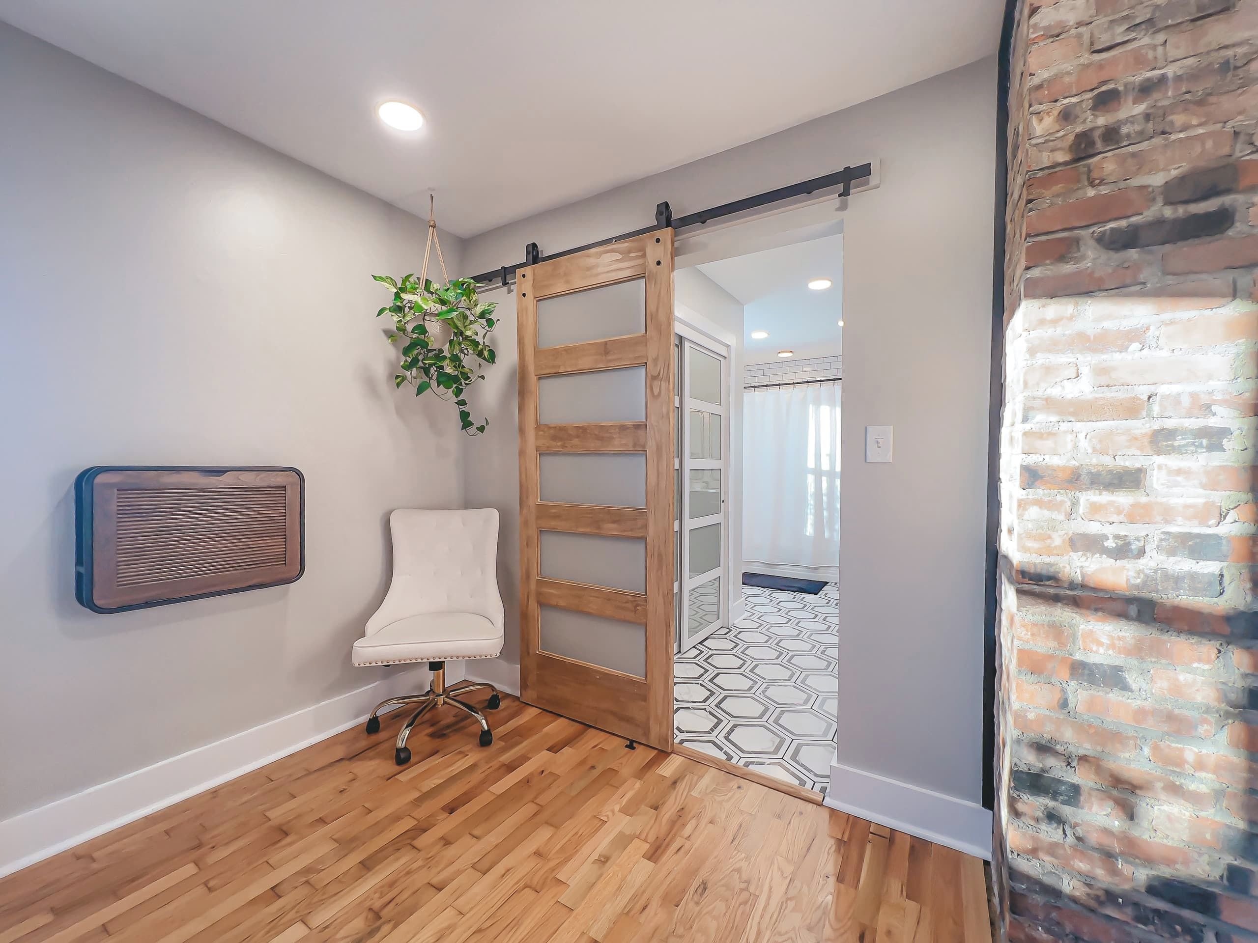 A room with a sliding door leading to a bathroom, a white chair, a hanging plant, and a radiator.