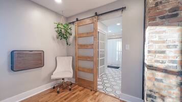 A room with a sliding door leading to a bathroom, a white chair, a hanging plant, and a radiator.