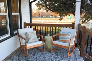 A porch with two wooden chairs and a small round table, a patterned rug, and a view of a fenced yard with trees. - [C] Private Country Retreat 10 Acres + 4 Min to Lawrence (Lawrence)