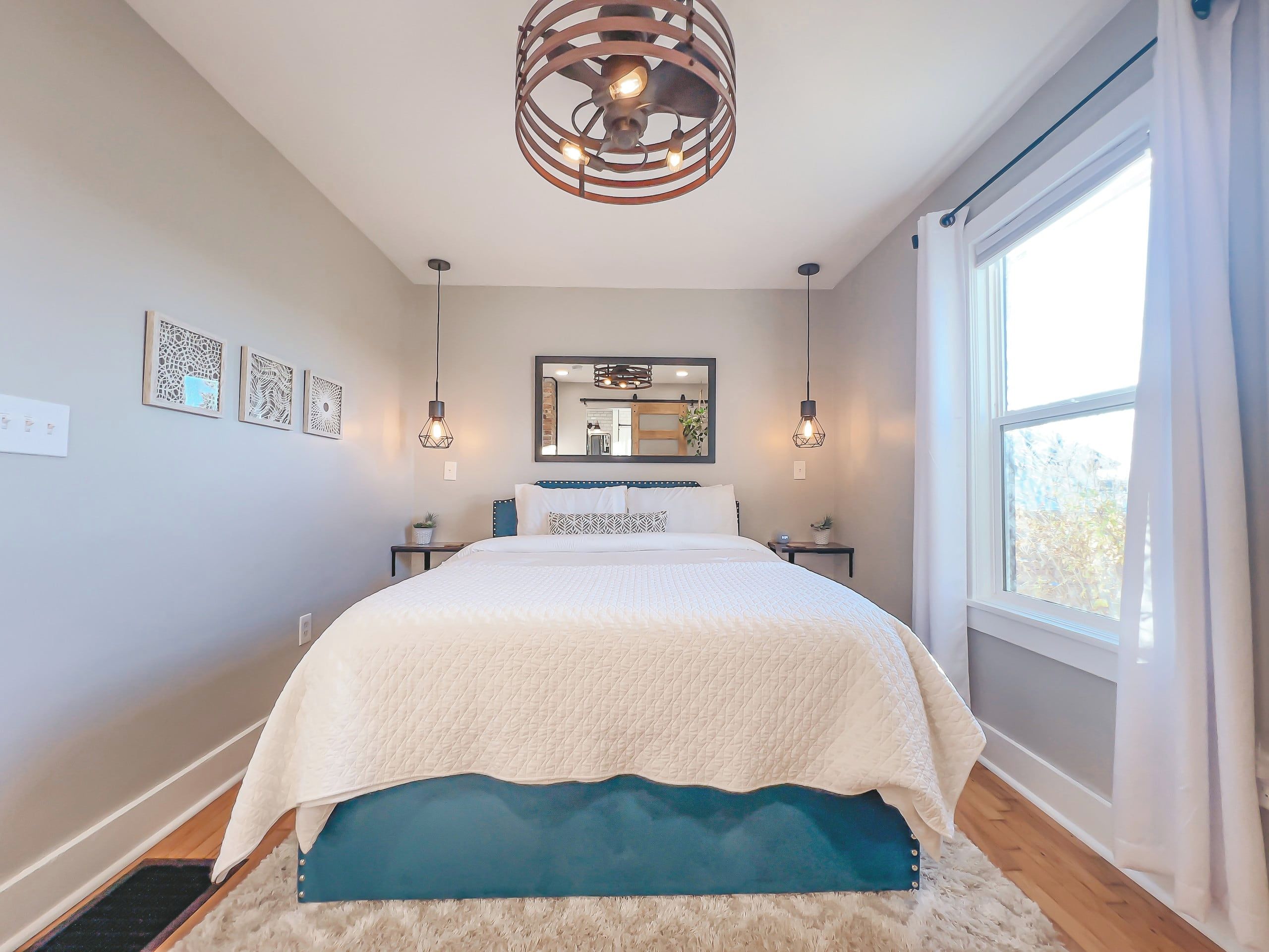 Un dormitorio con cama, mesitas de noche, un espejo y una ventana con cortinas.