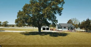 Une maison avec un garage, un grand arbre à l’avant et une cour clôturée.