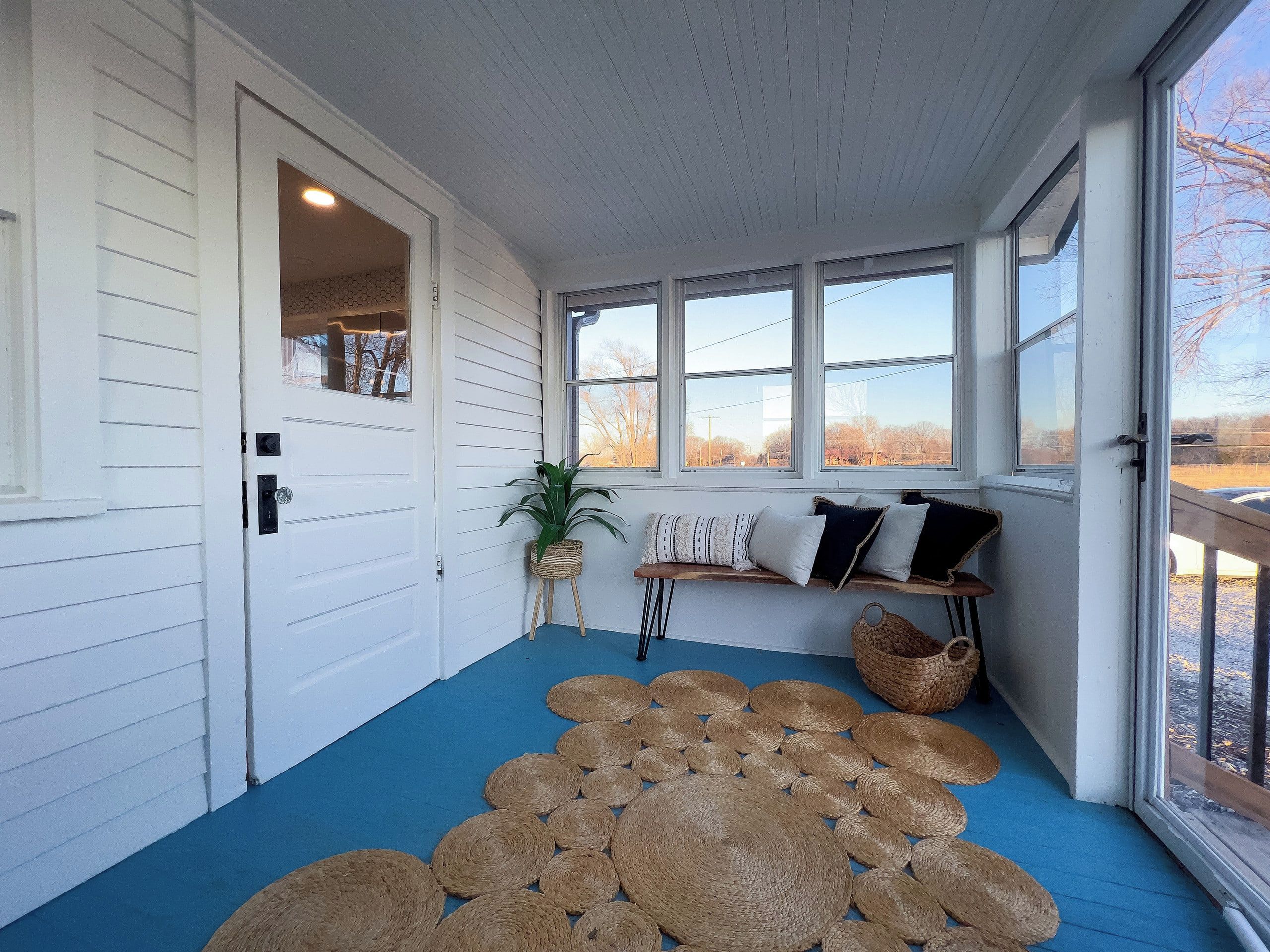 Een kamer met een blauwe vloer, een witte deur, een bank met kussens en een groot raam.