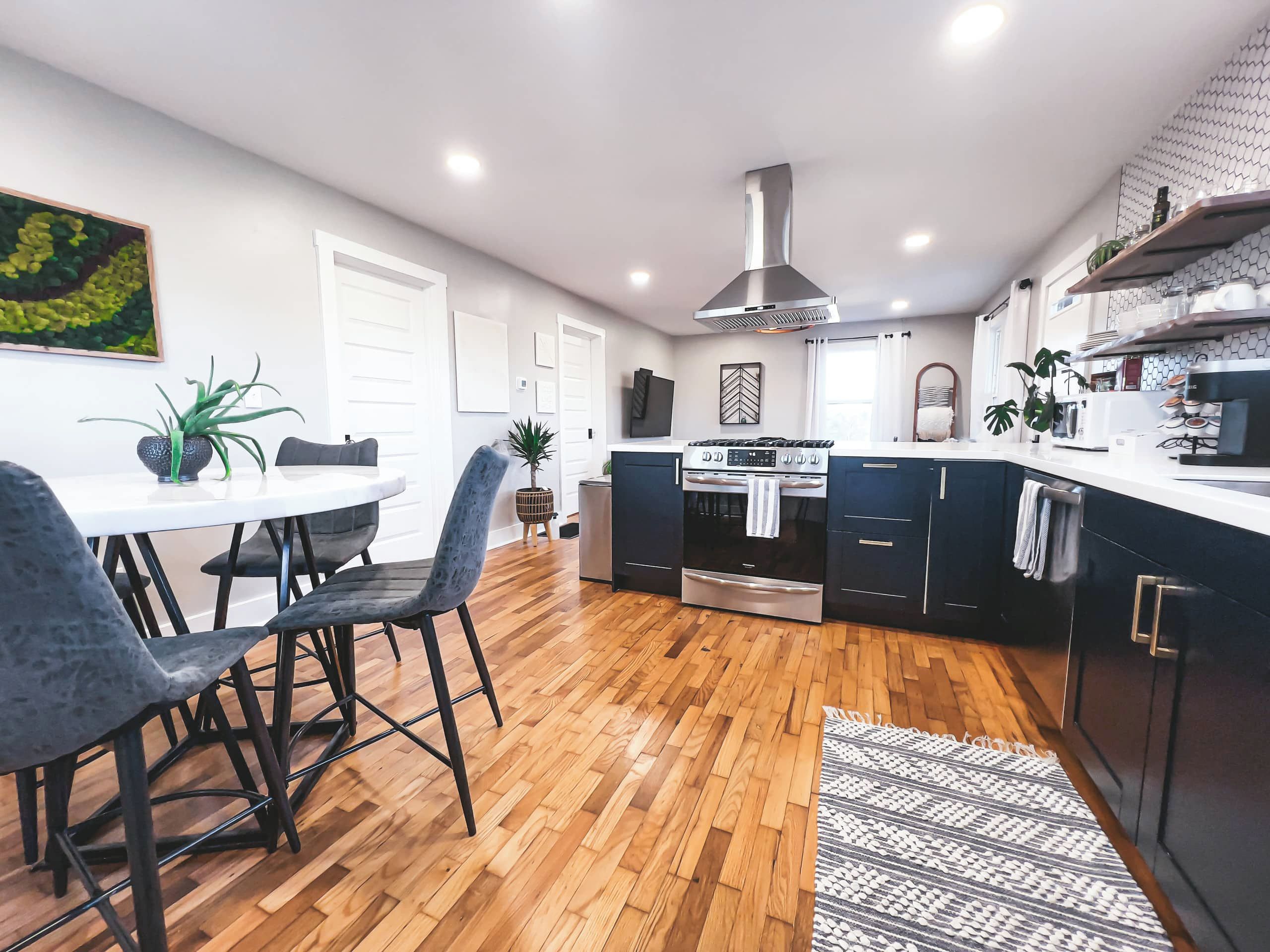 A modern kitchen with dark cabinetry, a central island, and a dining area with a round table and chairs.