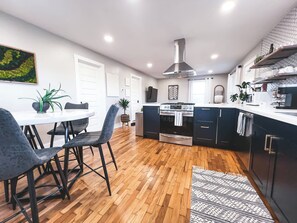 Une cuisine moderne avec des meubles de couleur sombre, un îlot central et un coin repas comprenant une table ronde et des chaises.