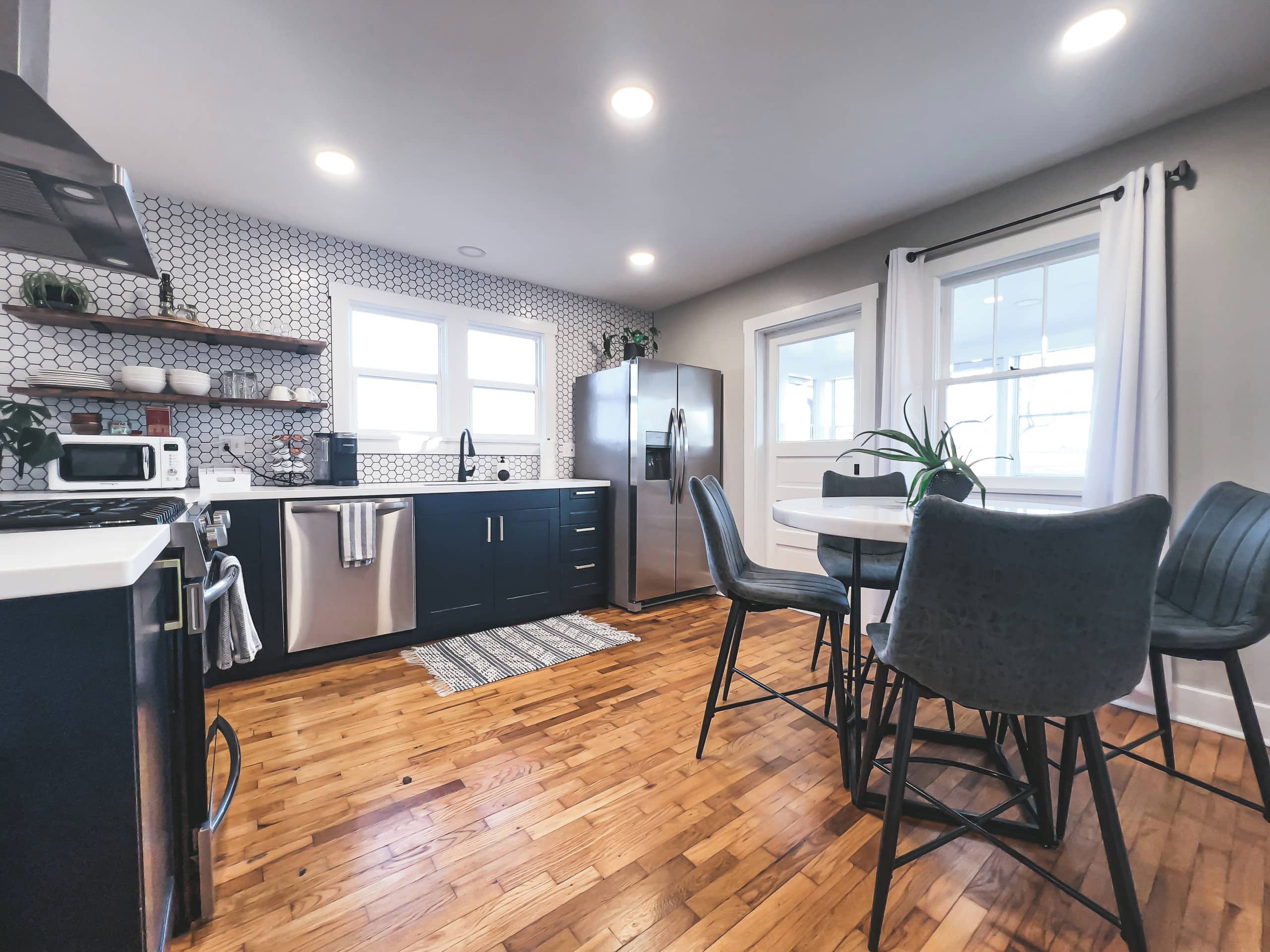 A modern kitchen with wooden flooring, a dining area with two chairs, and a refrigerator.