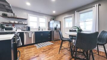 A modern kitchen with wooden flooring, a dining area with two chairs, and a refrigerator.