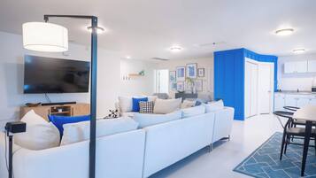 Un salon moderne avec un canapé blanc, un téléviseur à écran plat et un coin repas comprenant une table et des chaises.