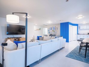 Una sala de estar moderna con un sofá blanco, un televisor de pantalla plana y un comedor con mesa y sillas.
