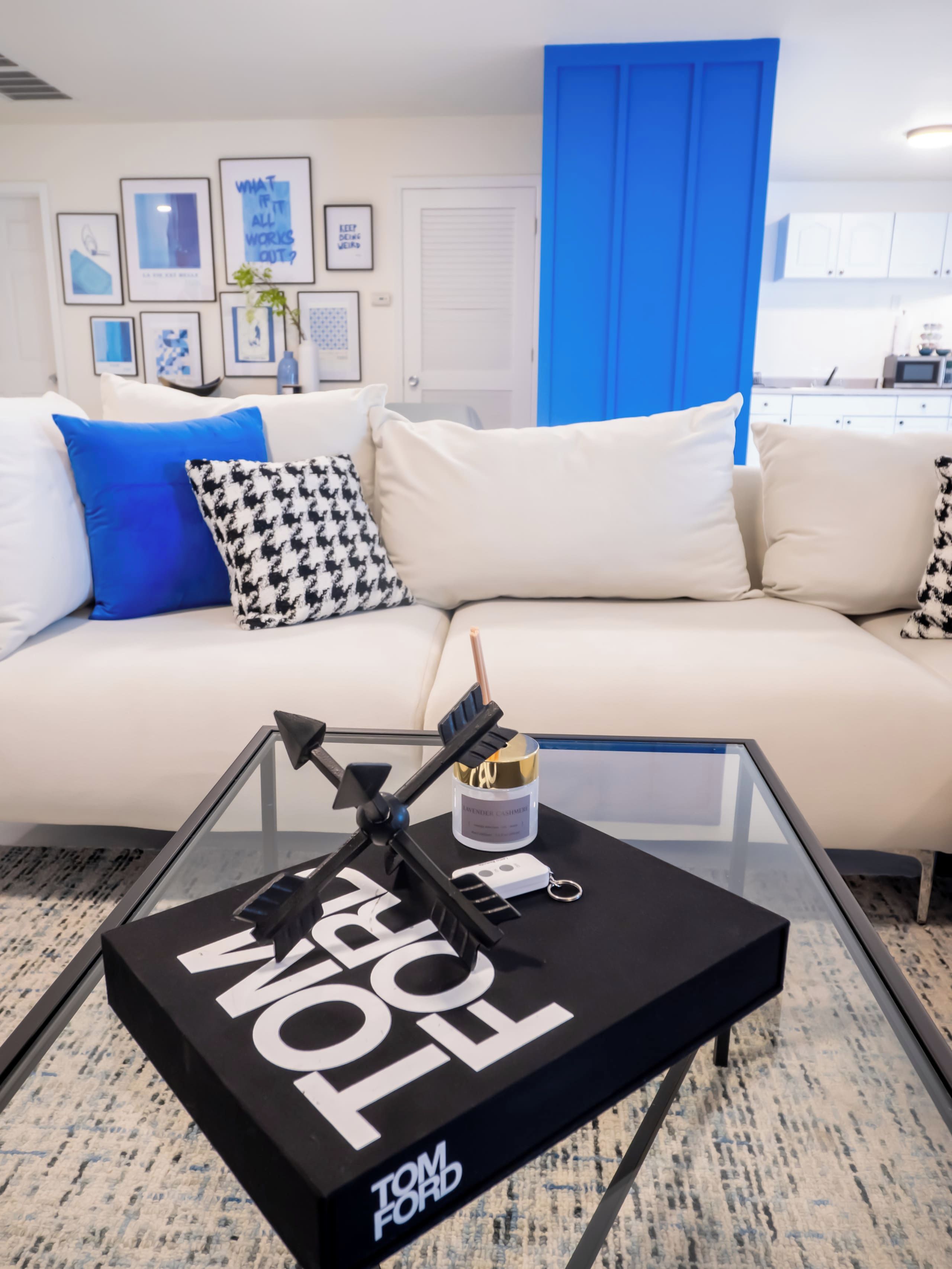 A modern living room with a glass coffee table, a sofa with patterned cushions, and a blue accent wall.