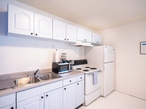 A kitchen with white cabinets, a stainless steel sink, a microwave, a stove, and a refrigerator.