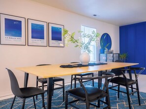 A conference room with a long table, four chairs, framed artwork on the wall, a potted plant, and a blue accent wall.