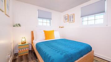 Une chambre à coucher avec un lit, une table de chevet avec une lampe et deux fenêtres équipées de stores.