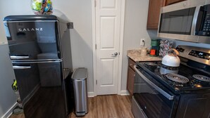 A compact kitchen with a black Galanz refrigerator, a stainless steel trash bin, a microwave, and a stove. - [1] StayAwhile: The Pink Retreat. 2-Min Walk to Mass! (Lawrence)