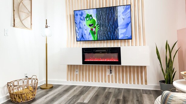 A modern living room with a flat-screen TV mounted on a wooden wall, a floor lamp, a woven basket, and a potted plant. - [1] StayAwhile: The Pink Retreat. 2-Min Walk to Mass! (Lawrence)