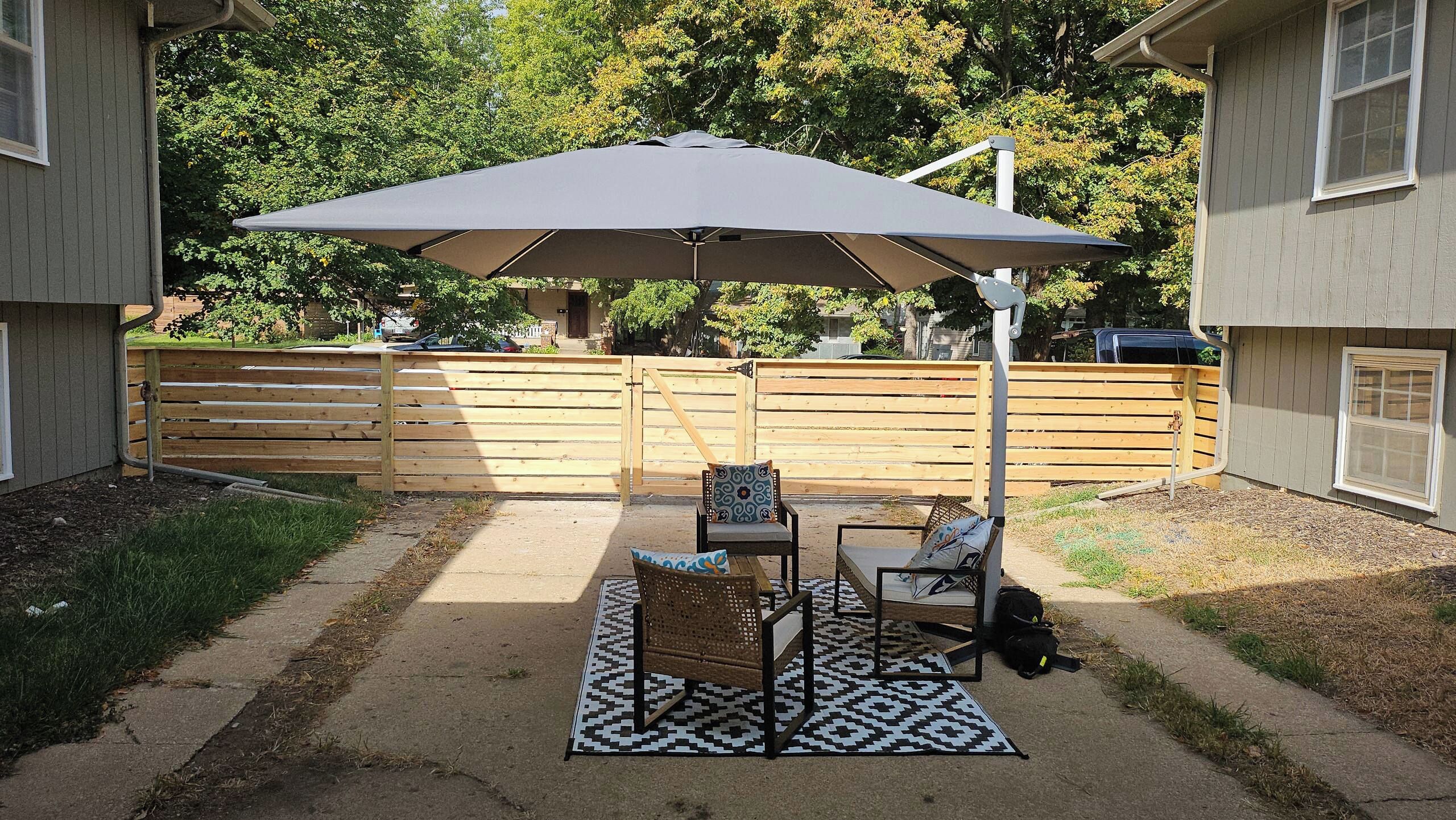 An outdoor patio with a table and chairs, a large umbrella, and a patterned rug.