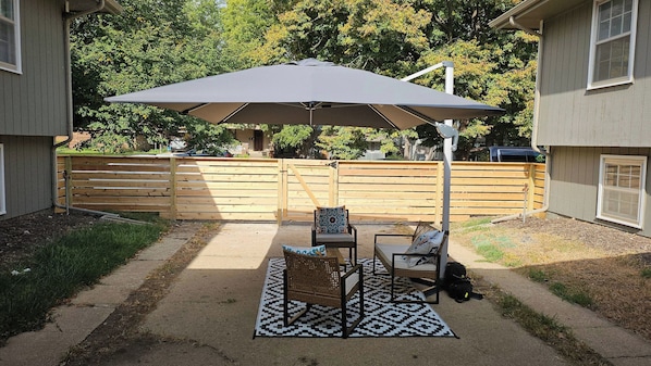 Un patio esterno con tavolo e sedie, un ombrellone grande e un tappeto decorato.