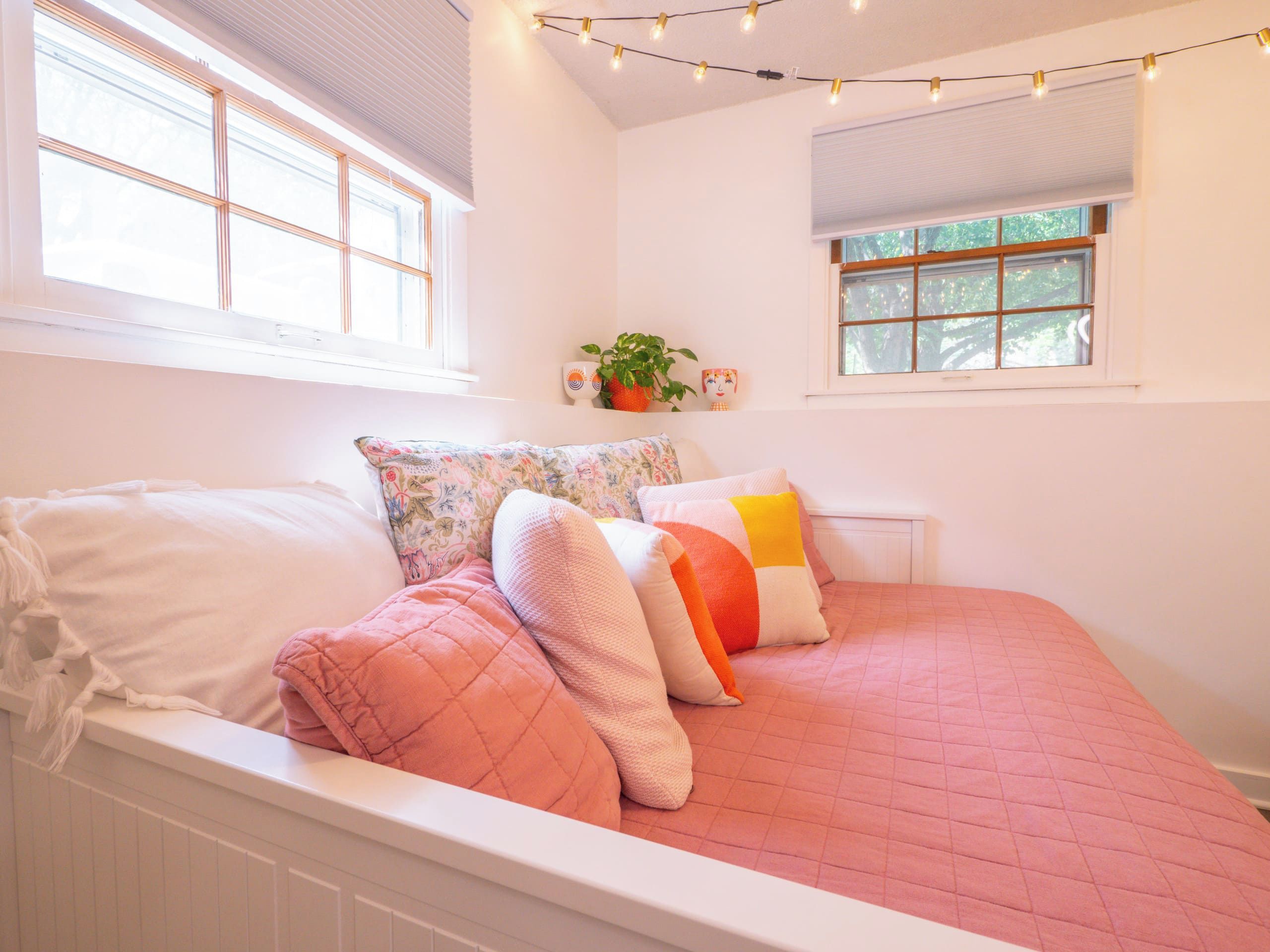 A bedroom with a bed, pillows, a window, and string lights.