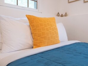 A bed with white and blue bedding, a yellow pillow, and three wall-mounted vases.