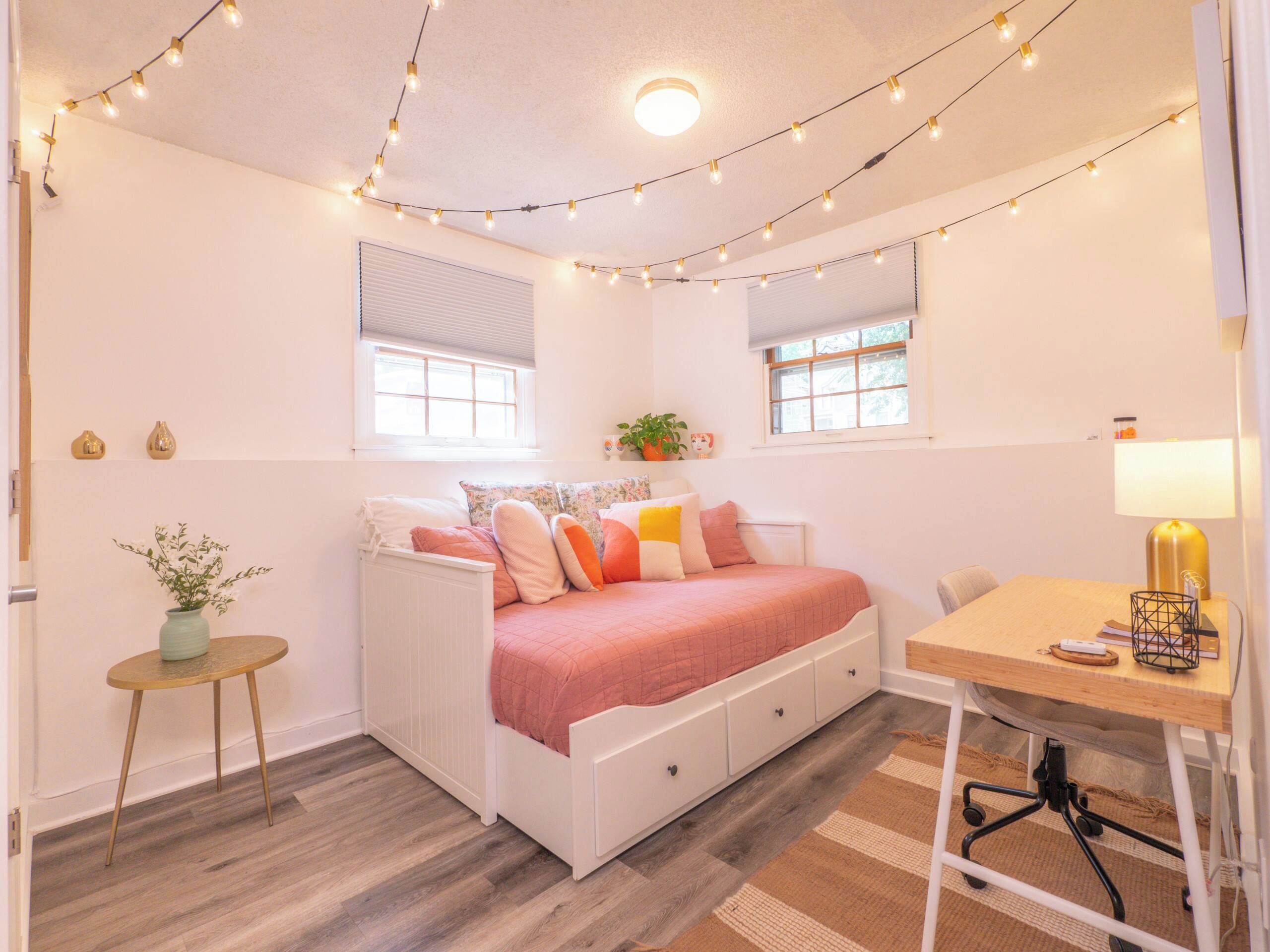A bedroom with a bed, bedside table, lamp, and a small table with a plant.