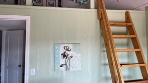 A room with a light green wall, a wooden ladder, and a framed artwork of flowers. - The Redbud ~ Cabin Seventeen ~ Lake View ~ Pet Friendly (Royal)