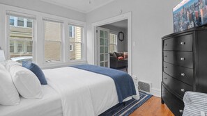 A bedroom with a bed, a dresser, and a door leading to another room.