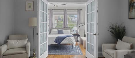 A bedroom with a bed, a chair, a desk, and a plant.