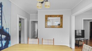 A dining room with a wooden table, two chairs, a mirror with a decorative frame, and a television on a stand.