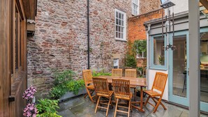 A stone building with a wooden table and chairs, a small garden, and a blue door.