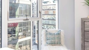 Une chambre moderne avec une grande fenêtre, un fauteuil moelleux doté d’un coussin et un meuble en bois.
