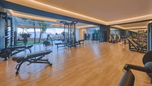 A spacious gym with various exercise equipment, large windows, and a wooden floor.