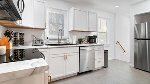 A modern kitchen with white cabinets, stainless steel appliances, and a marble countertop. - Urban Oasis: A Charming Downtown Retreat with Game Room, Firepit and Yard Games (Evansville)