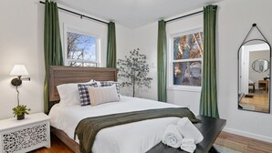 A neatly arranged bedroom with a bed, bedside table, lamp, and a mirror. - Urban Oasis: A Charming Downtown Retreat with Game Room, Firepit and Yard Games (Evansville)