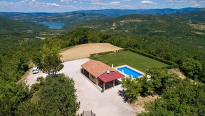Ein Haus mit rotem Dach, einem Swimmingpool und Blick auf einen See und Berge.