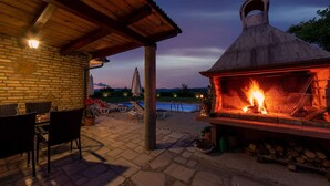 Eine Außenpatio mit Kamin aus Stein, Liegestühlen und einem Pool im Hintergrund.