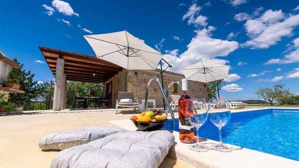 Ein Poolbereich mit blauem Himmel, einem Pool und Sonnenschirmen, die Schatten spenden.