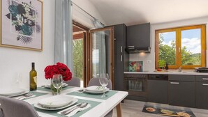Eine moderne Küche mit dunklen Schränken, ein Essbereich mit Tisch für zwei Personen und ein großes Fenster mit Blick auf Grünflächen.