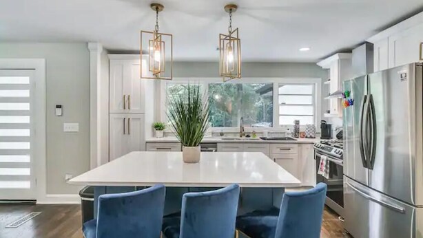 Une cuisine moderne dotée d’un grand îlot central, d’appareils électroménagers en acier inoxydable et de chaises bleues.