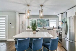A modern kitchen with a large island, stainless steel appliances, and blue chairs. - Designer 5 Bedroom with Backyard Downtown ATL (Atlanta)