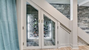 Un escalier menant à une pièce dont un mur est en pierre et qui possède une porte en verre derrière laquelle on peut voir des bouteilles.