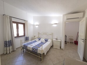 A bedroom with a bed, bedside tables, a window with curtains, a door, and an air conditioning unit.